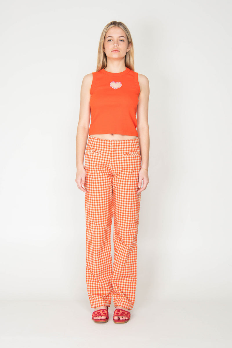 Woman wearing an orange sleeveless top and checkered pants on a white background