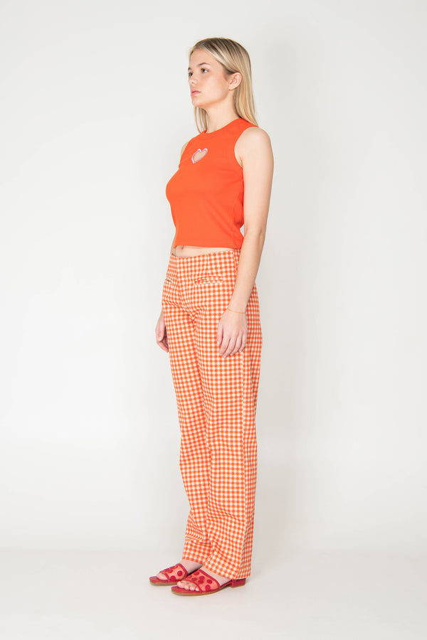 Woman wearing an orange sleeveless top and checkered pants on a white background