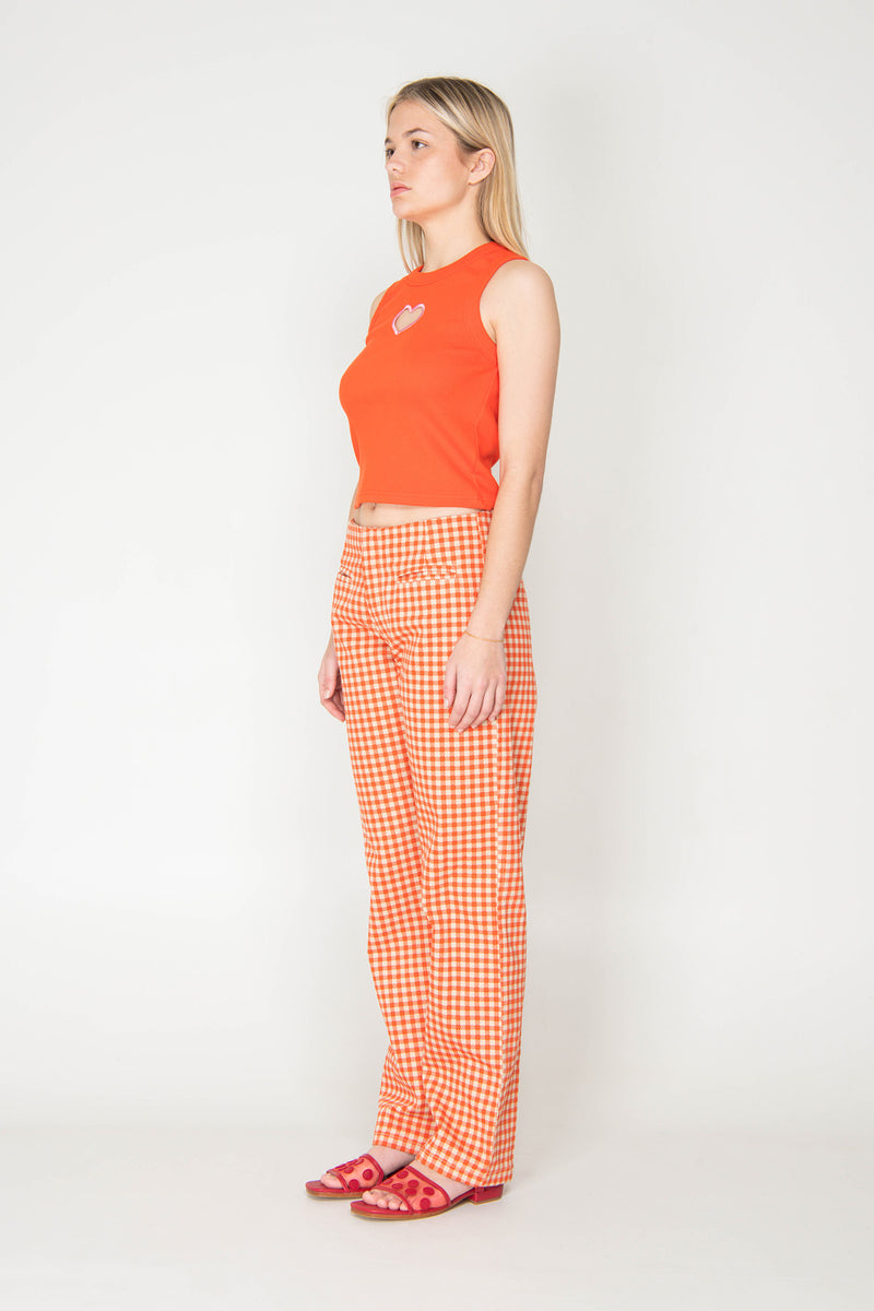 Woman wearing an orange sleeveless top and checkered pants on a white background