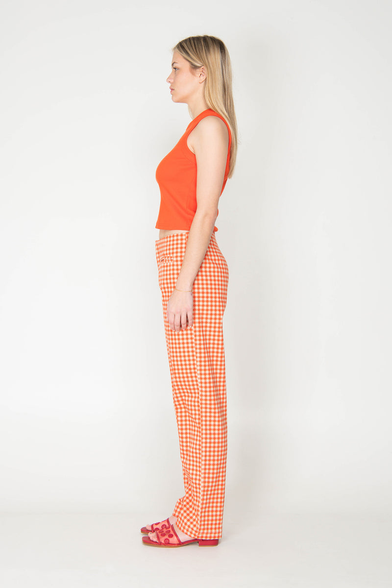 Woman wearing an orange sleeveless top and checkered pants on a white background