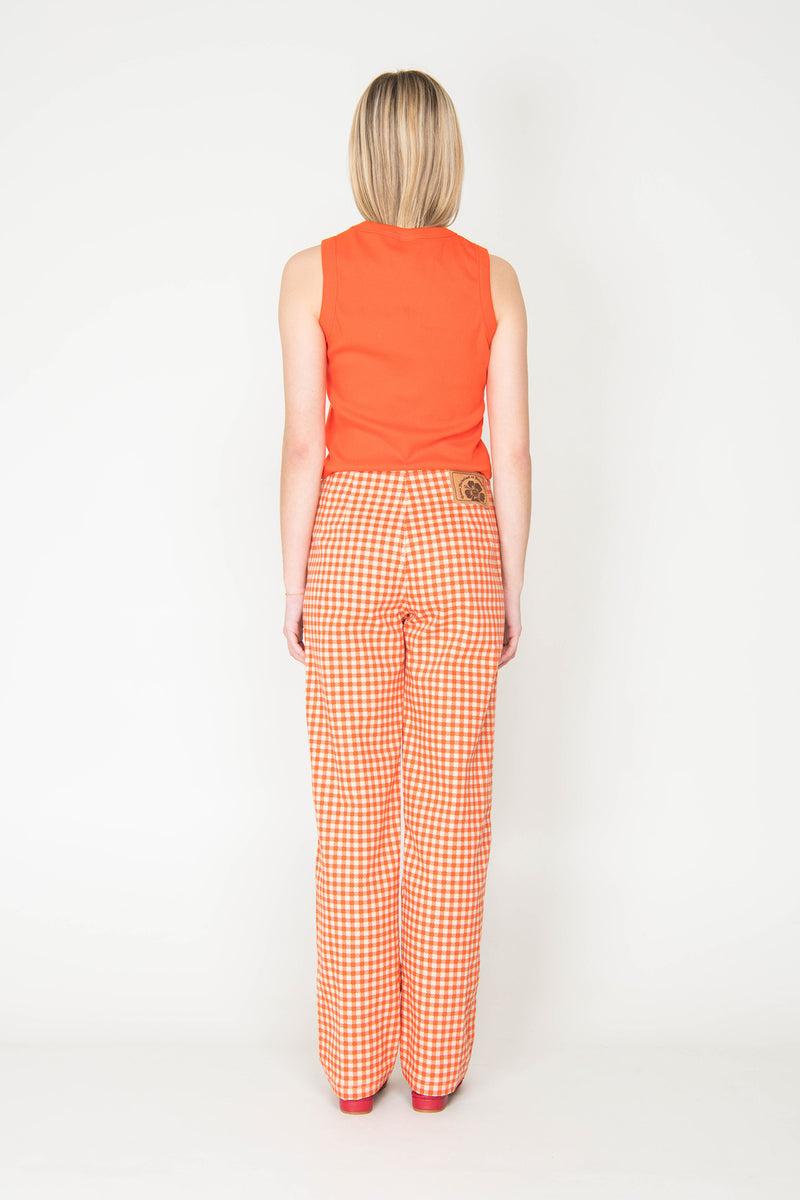 Woman wearing an orange sleeveless top and checkered pants on a white background