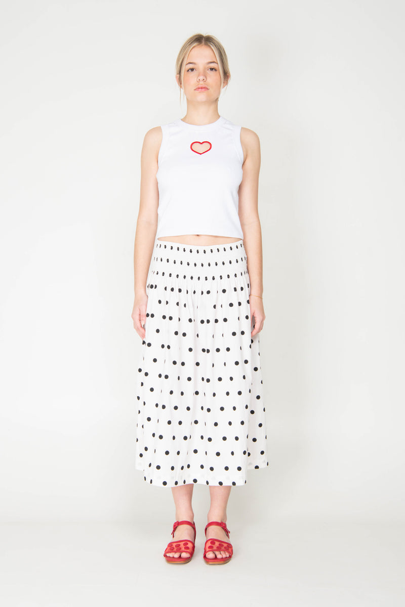 Woman wearing a white sleeveless top with a red heart and a polka dot skirt on a white background