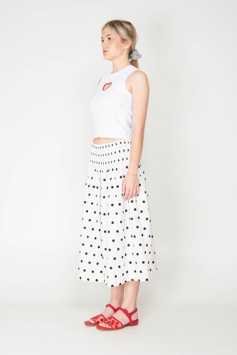 Woman wearing a white sleeveless top with red accents and a black and white polka dot skirt on a white background