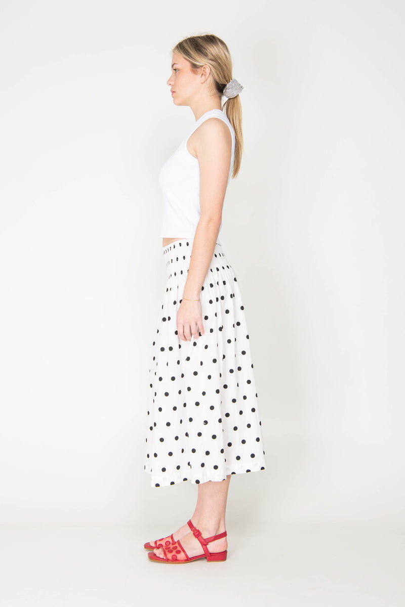 Woman wearing a white sleeveless top and polka dot skirt on a white background