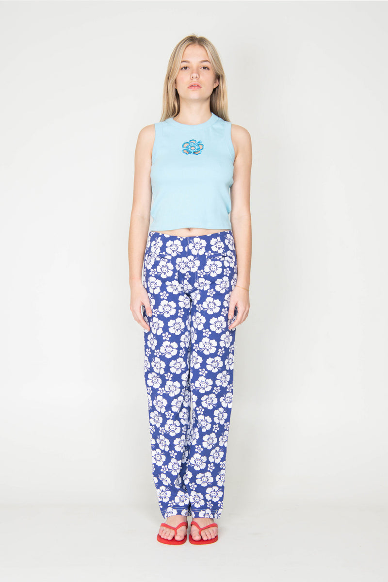 Woman wearing a light blue sleeveless top and blue floral pants on a white background