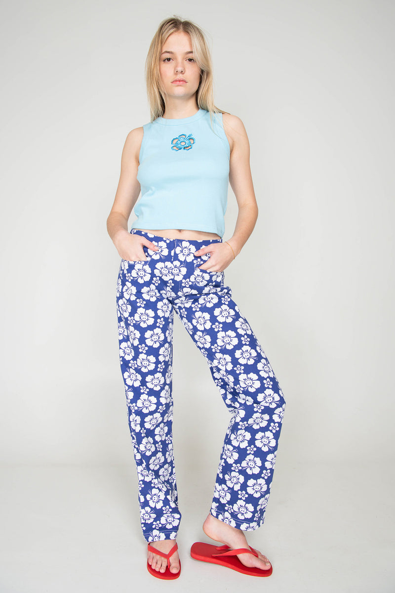 Woman wearing a light blue sleeveless top and blue floral pants on a white background