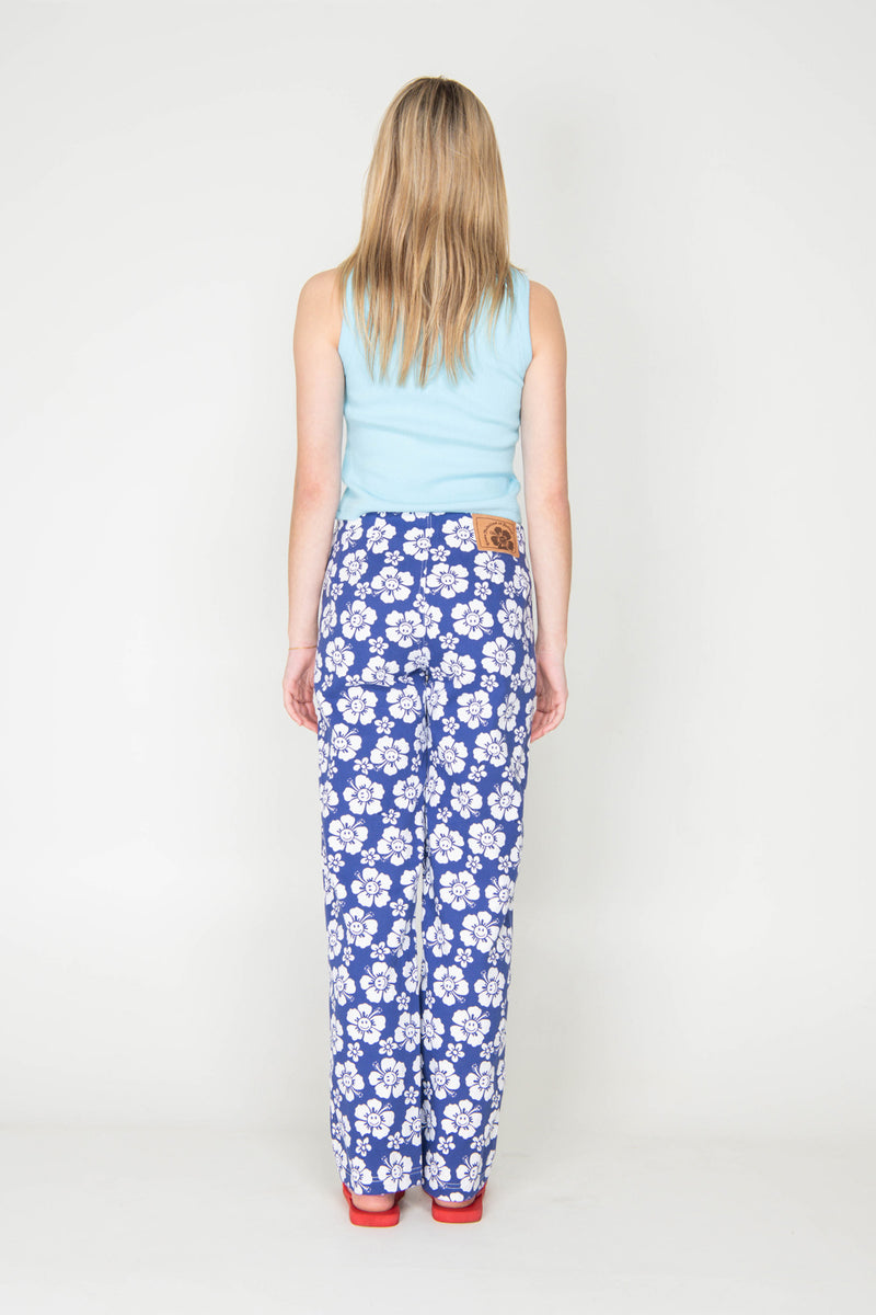 Woman wearing a light blue sleeveless top and blue floral pants on a white background
