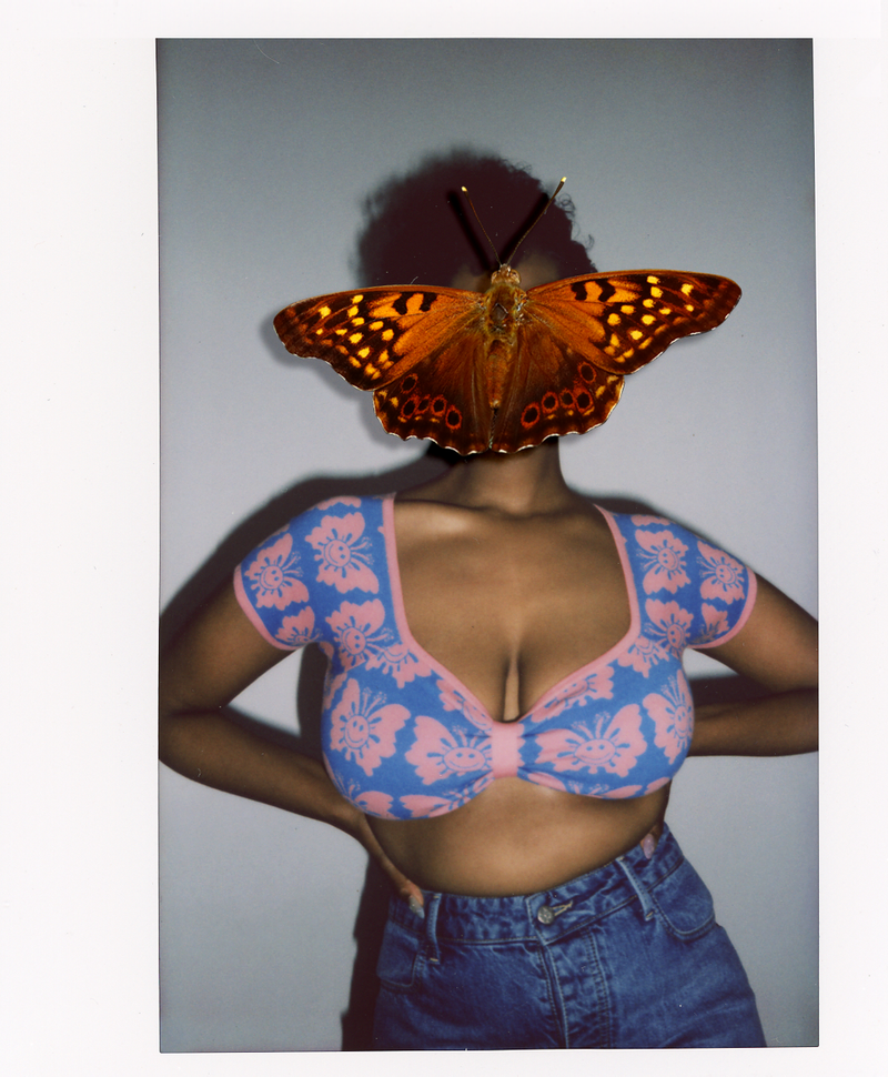 Person wearing a blue and pink floral top with a butterfly on their back against a plain background