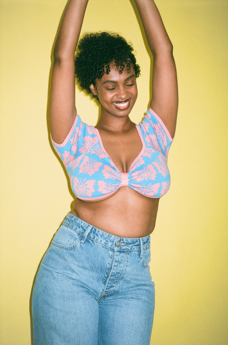 Woman wearing a pink lace top and blue jeans against a yellow background