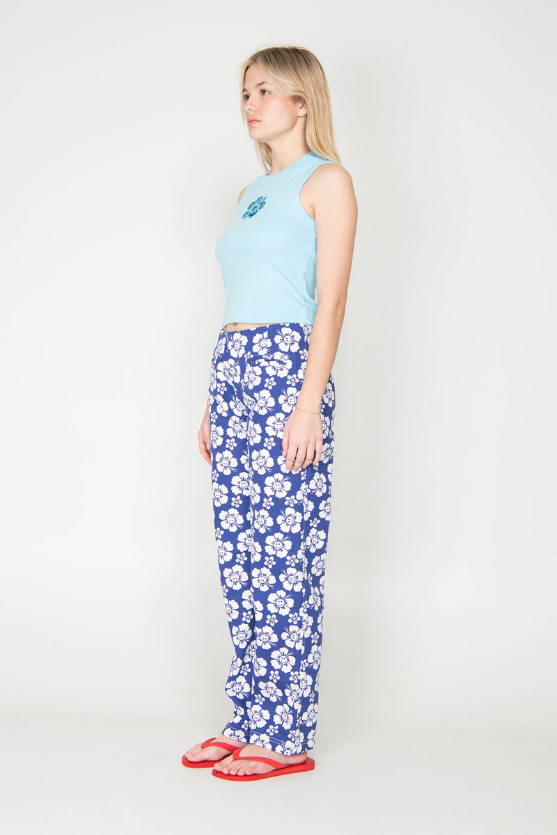Woman wearing a light blue sleeveless top and blue floral pants on a white background