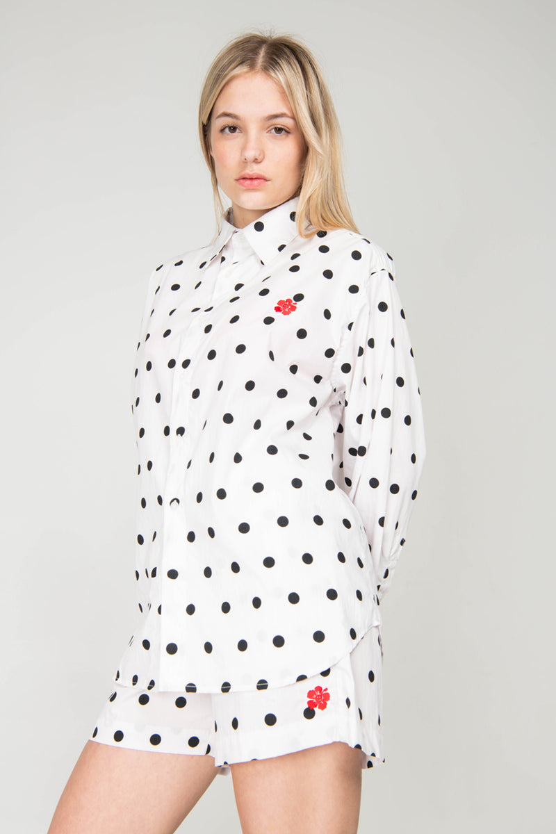 Woman wearing a white shirt with black polka dots and red flowers on a gray background