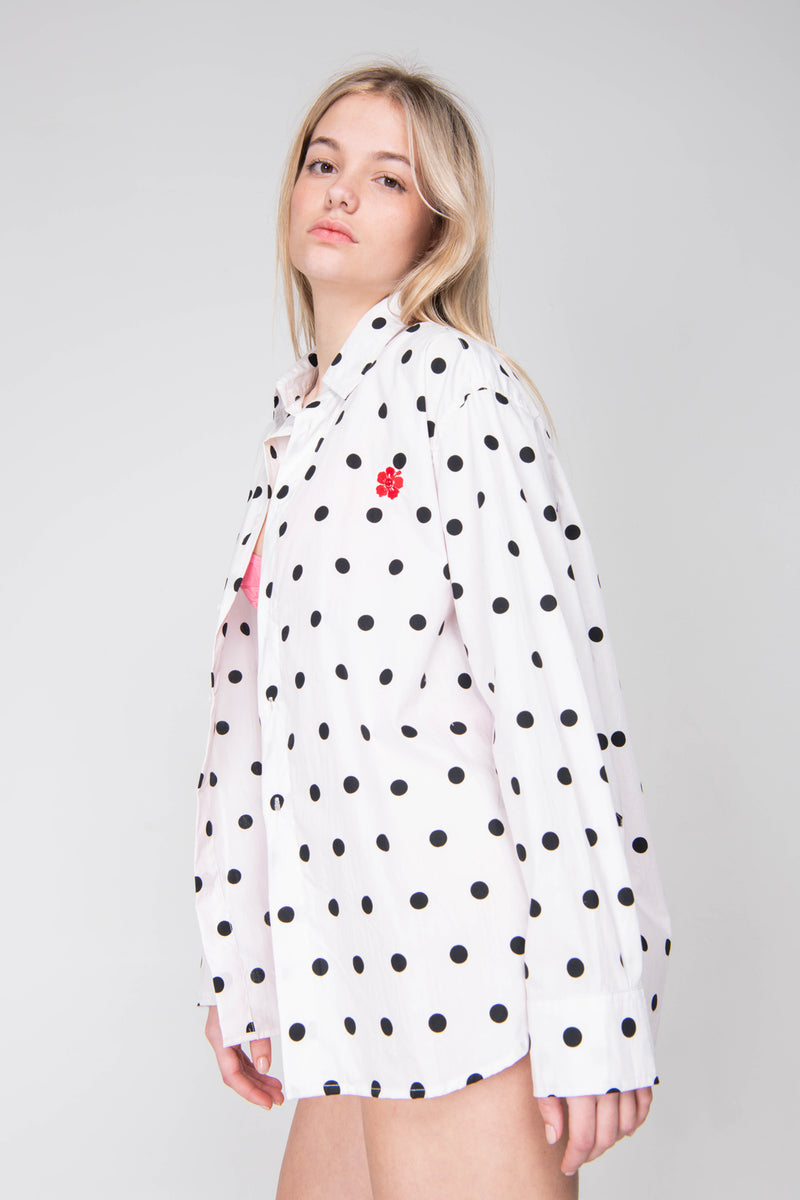 Woman wearing a white polka dot shirt with black dots on a plain background