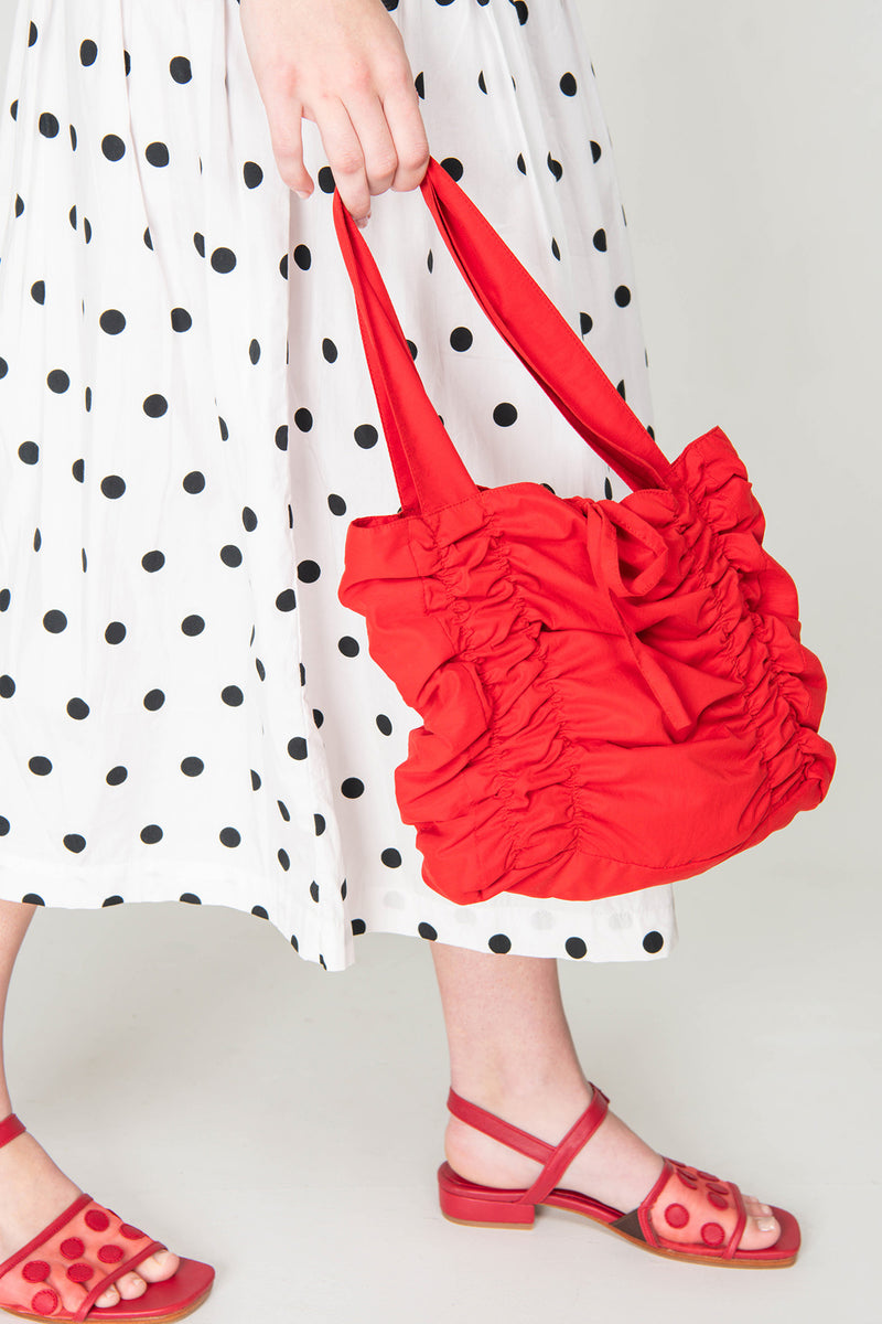 Person holding a red ruffled handbag wearing a polka dot dress and red sandals.