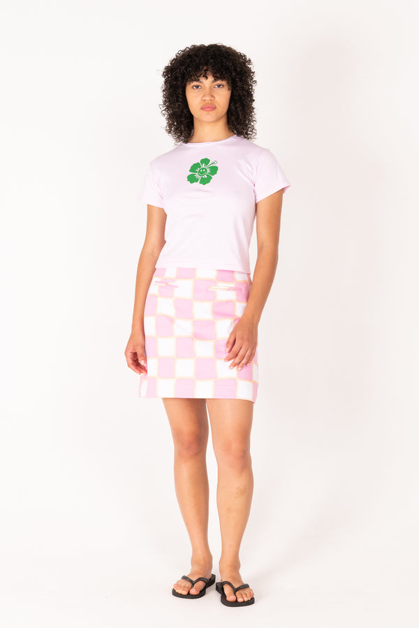 Person wearing a white t-shirt with a green logo and a pink checkered skirt on a white background