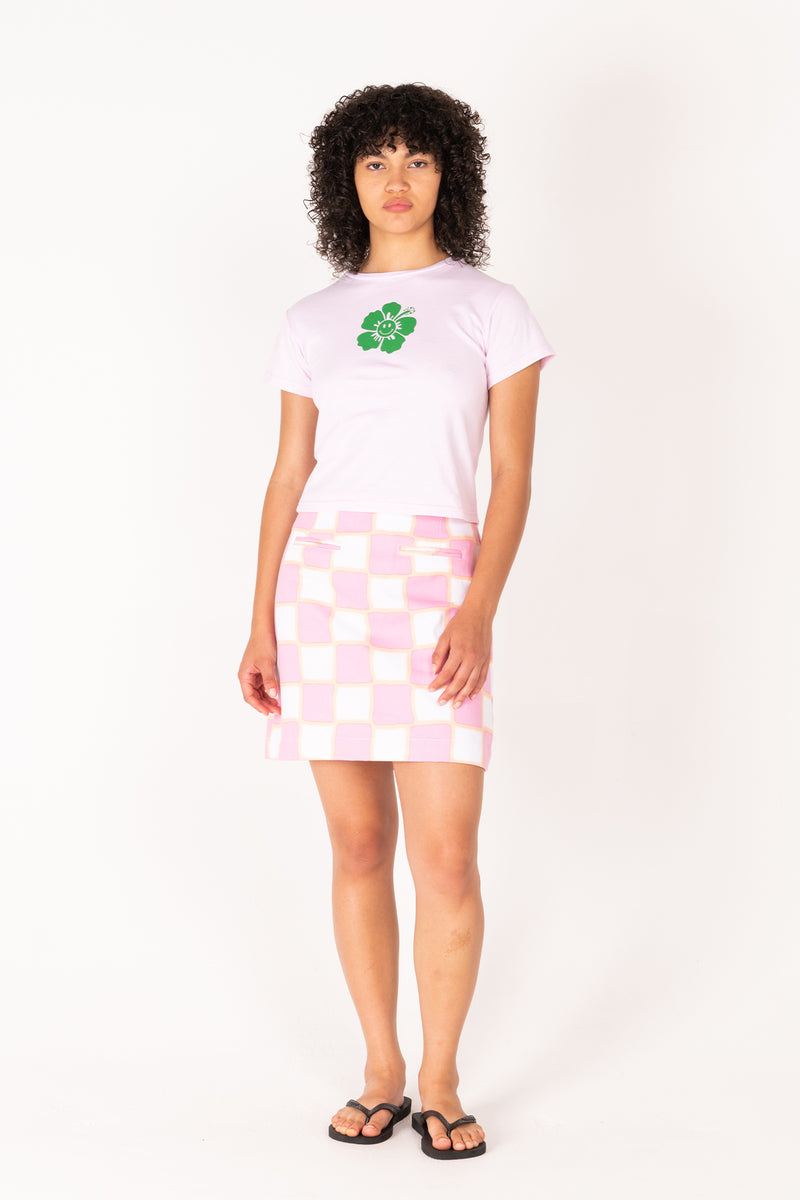 Person wearing a white t-shirt with a green logo and a pink checkered skirt on a white background