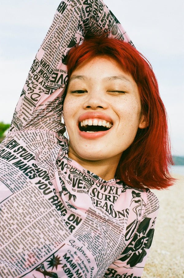 Person wearing a newspaper print hoodie with a smiley face, outdoors.
