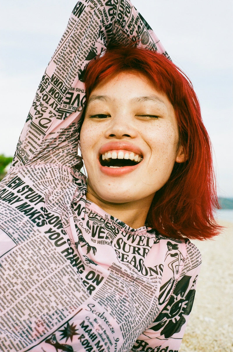 Person wearing a newspaper print hoodie with a smiley face, outdoors.