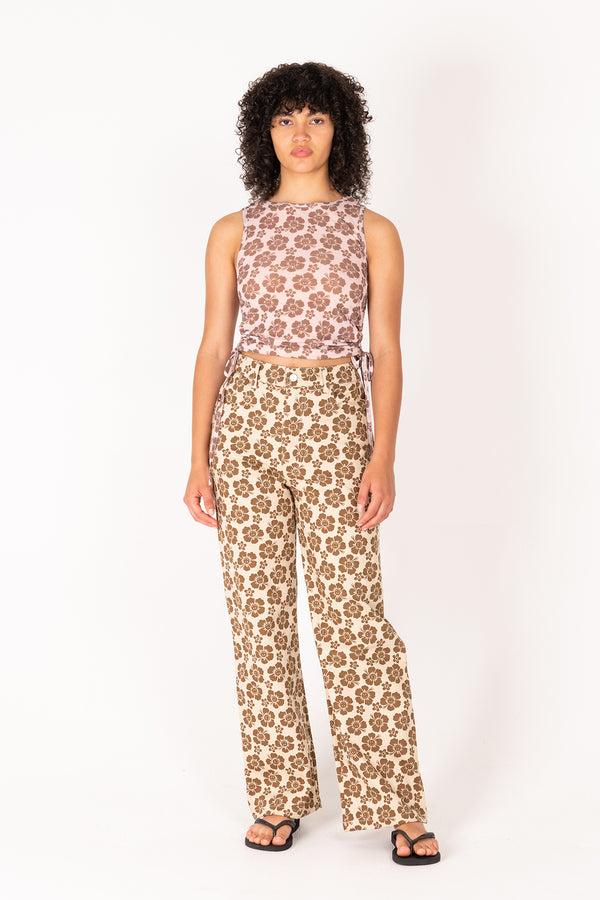 Woman wearing a sleeveless floral top and patterned pants on a white background