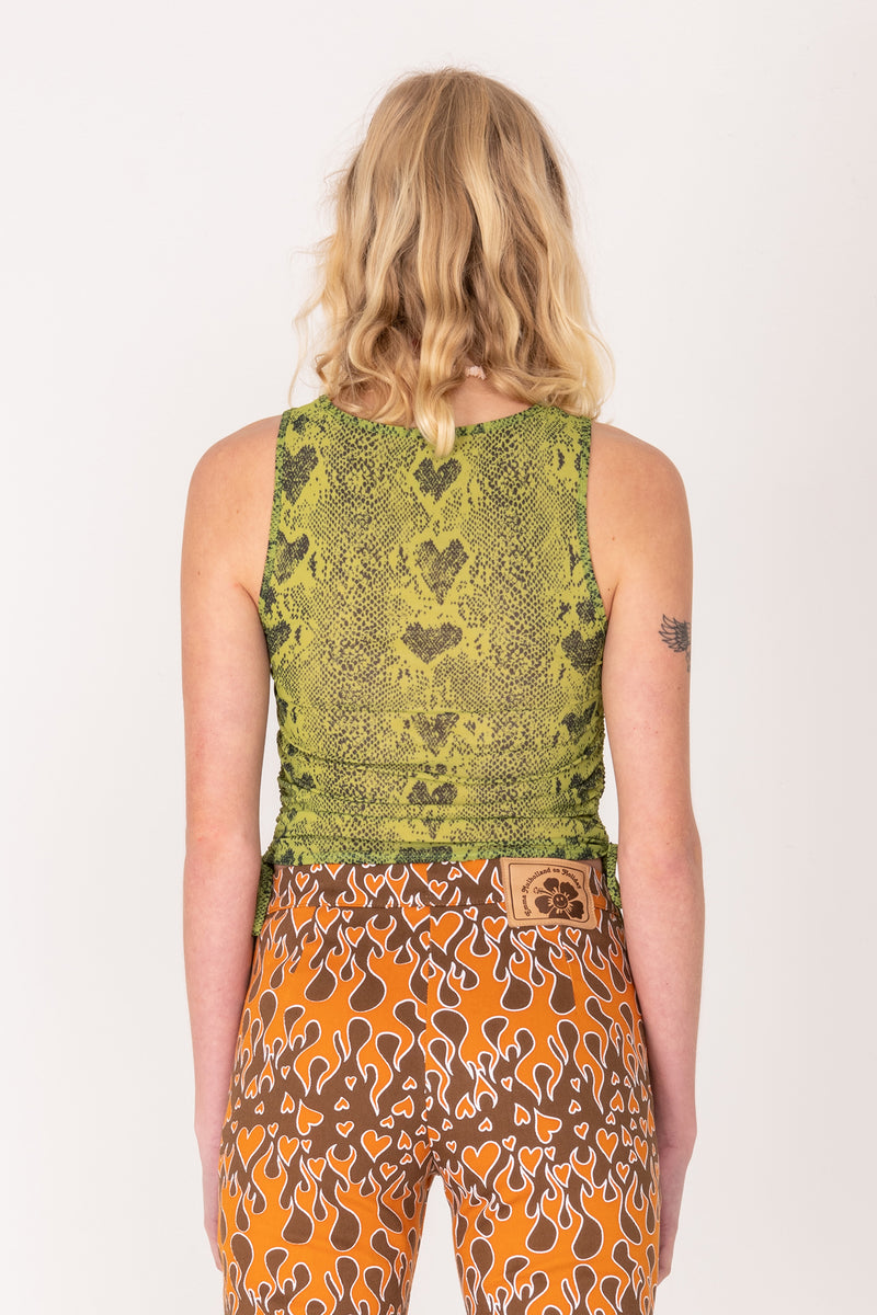 Person wearing a green patterned top and orange and brown pants on a white background