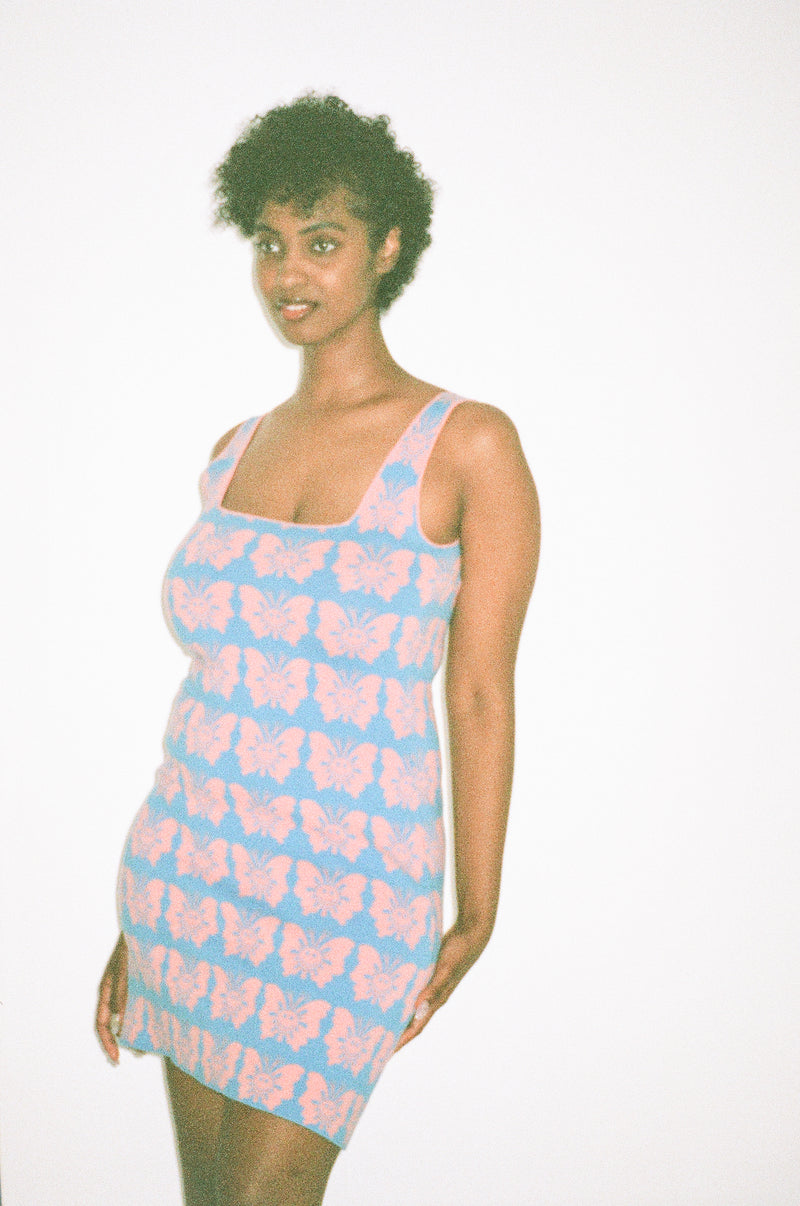 Woman wearing a light blue dress with pink butterfly patterns on a white background