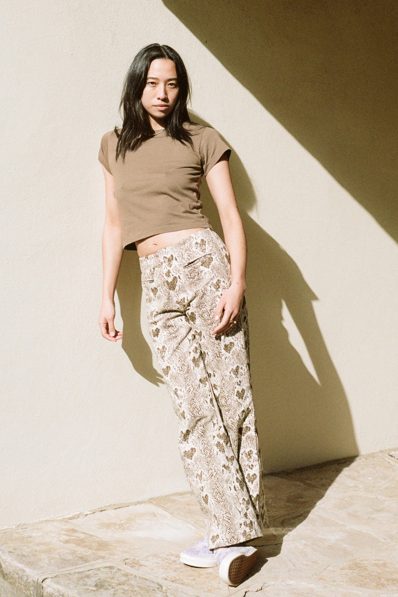 Woman wearing a brown crop top and patterned pants standing against a beige wall.