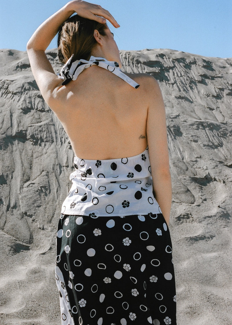 Woman wearing a black and white patterned dress standing on a rocky beach.
