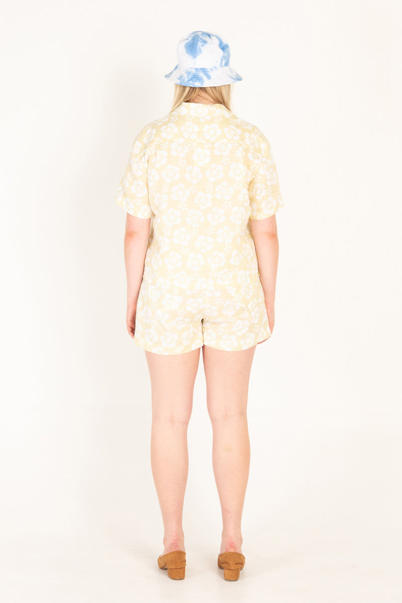 Person wearing a yellow patterned outfit with a tie-dye bucket hat on a white background