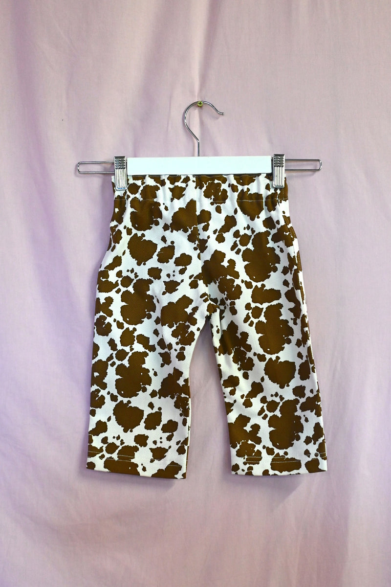 Cow print pants on a hanger against a light purple background