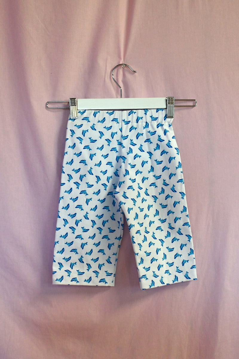 Shorts with blue dolphin pattern on a hanger against a pink background