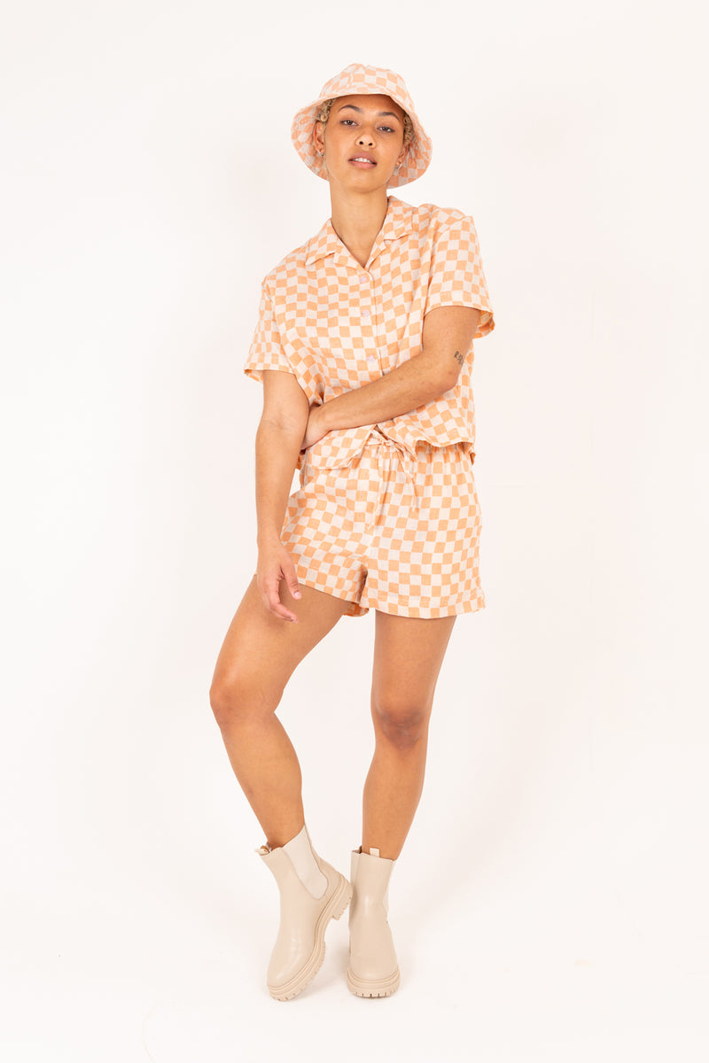 Woman wearing a matching orange and white checkered outfit with a hat on a white background