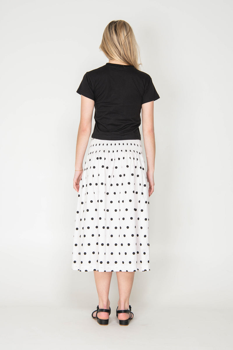 Person wearing a black t-shirt and white skirt with black polka dots on a white background