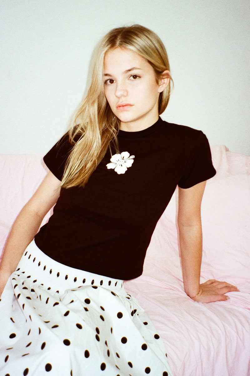 Woman wearing a black top with a white flower design and a polka dot skirt on a pink couch.
