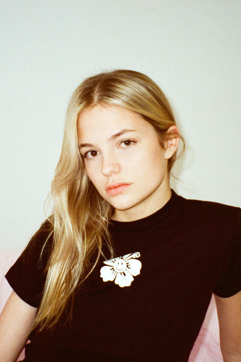 Woman wearing a black top with a floral brooch against a plain background