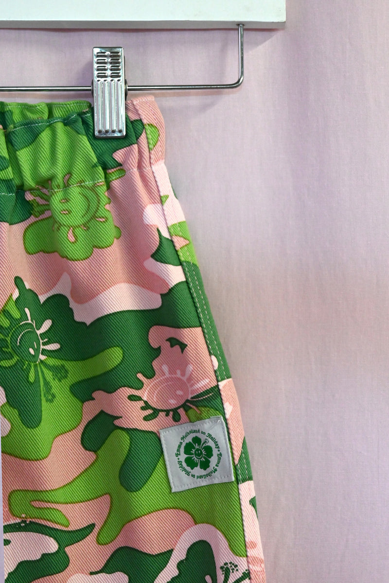 Kids pants with green camo pattern on a hanger against a light background