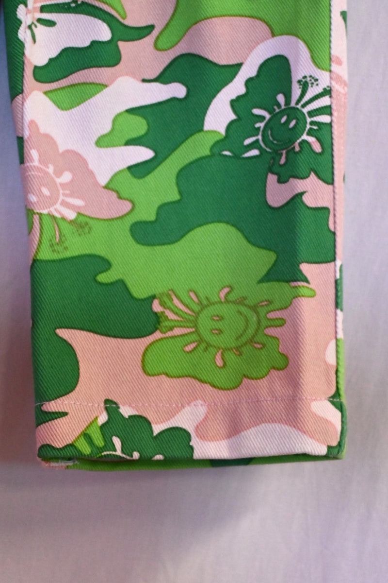 Kids pants with green camo pattern on a hanger against a light background