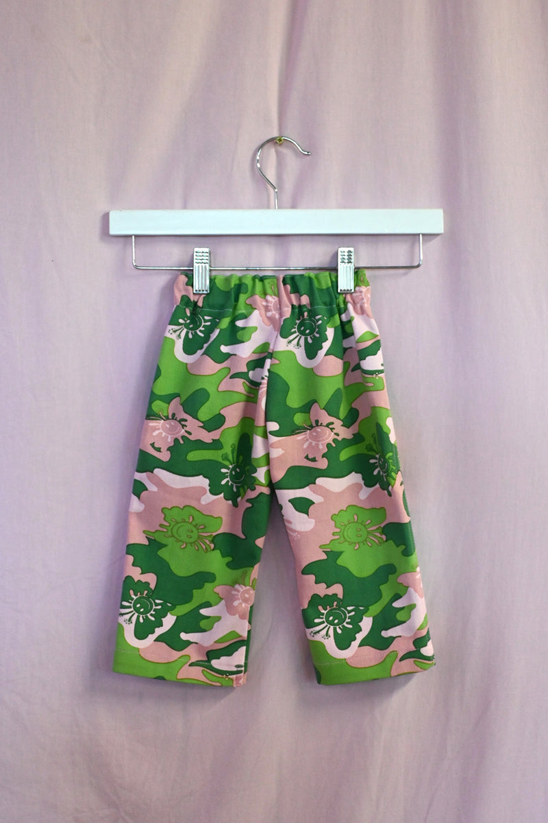 Kids pants with green camo pattern on a hanger against a light background