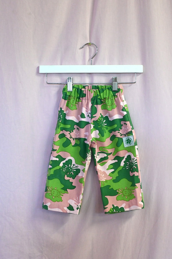 Kids pants with green camo pattern on a hanger against a light background