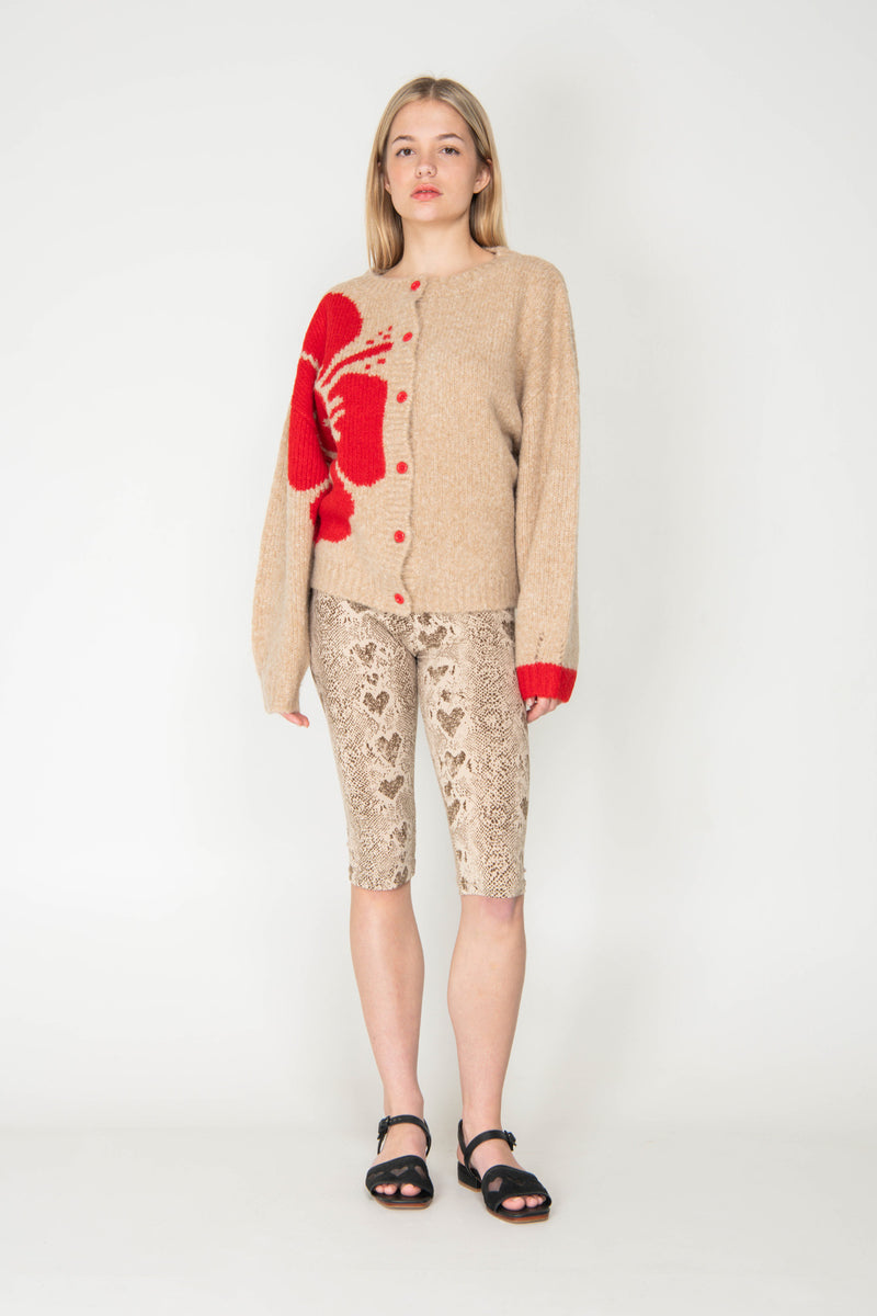 Woman wearing a beige cardigan with red accents and patterned pants on a white background