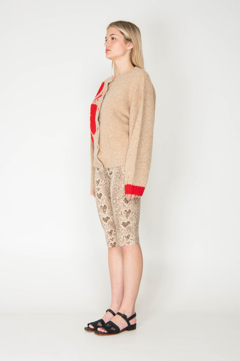 Woman wearing a beige cardigan with red trim and patterned pants on a white background