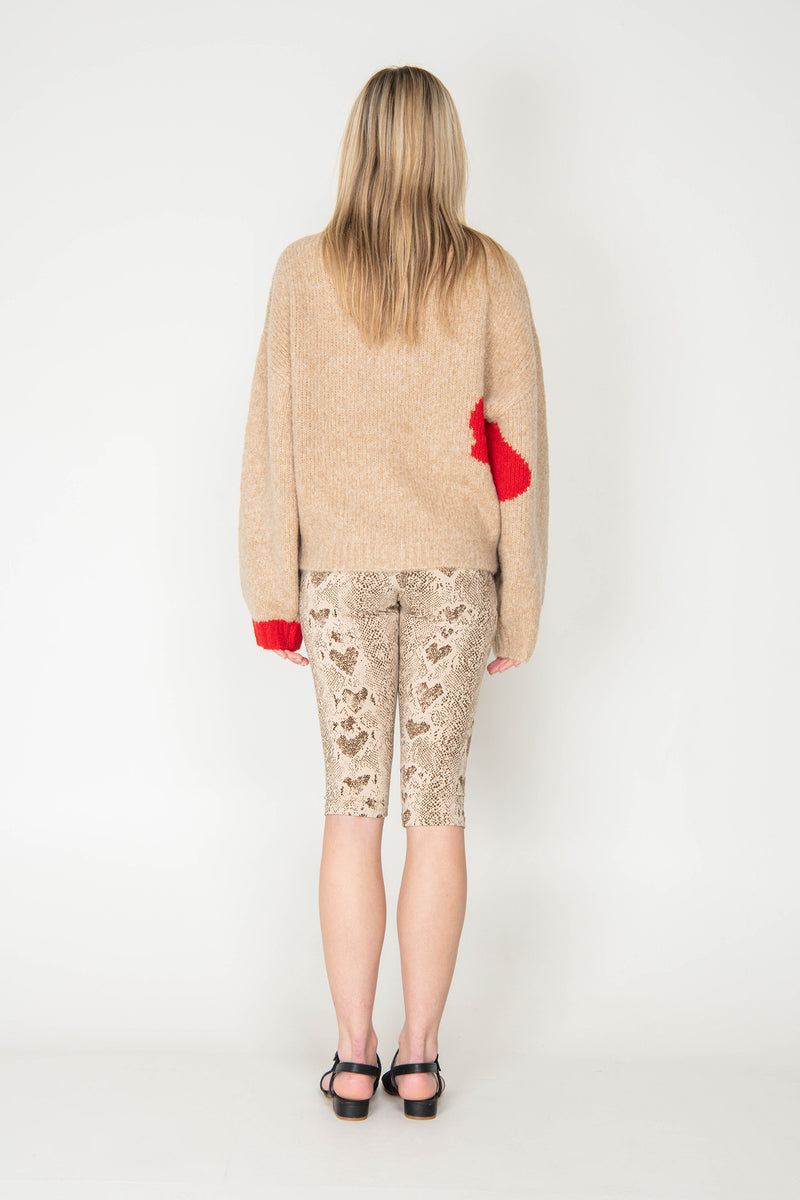 Woman wearing a beige sweater with red accents and patterned leggings on a white background