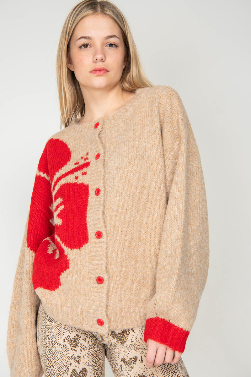 Woman wearing a beige cardigan with red accents on a plain background