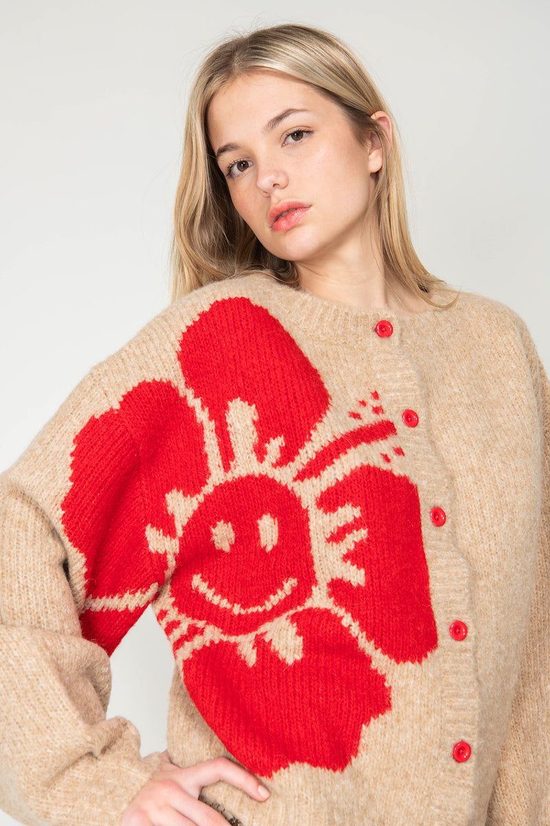 Woman wearing a beige sweater with a large red flower design on a plain background