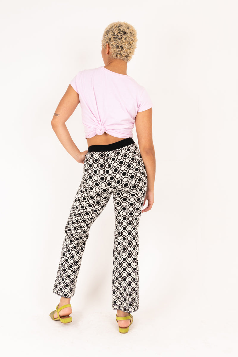 Person wearing a pink top and black and white patterned pants on a white background