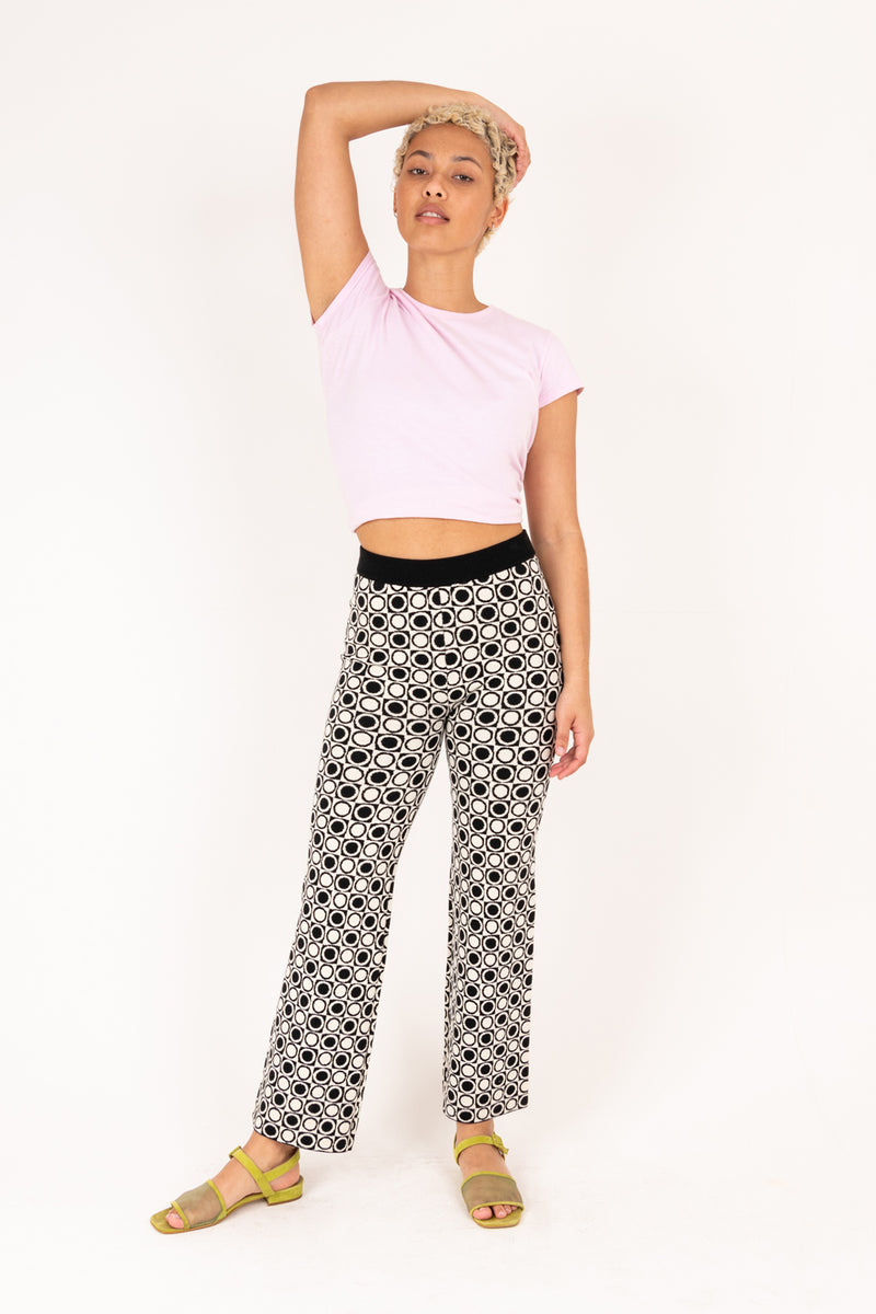 Woman wearing a light pink top and black and white patterned pants on a white background
