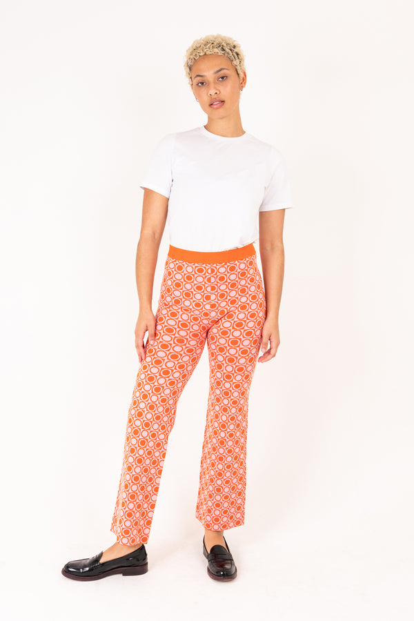 Woman wearing a white top and orange patterned pants on a white background