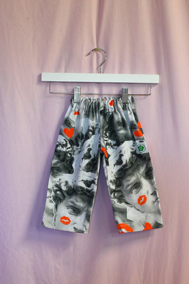 Pants with a david pattern and orange accents on a hanger against a pink background