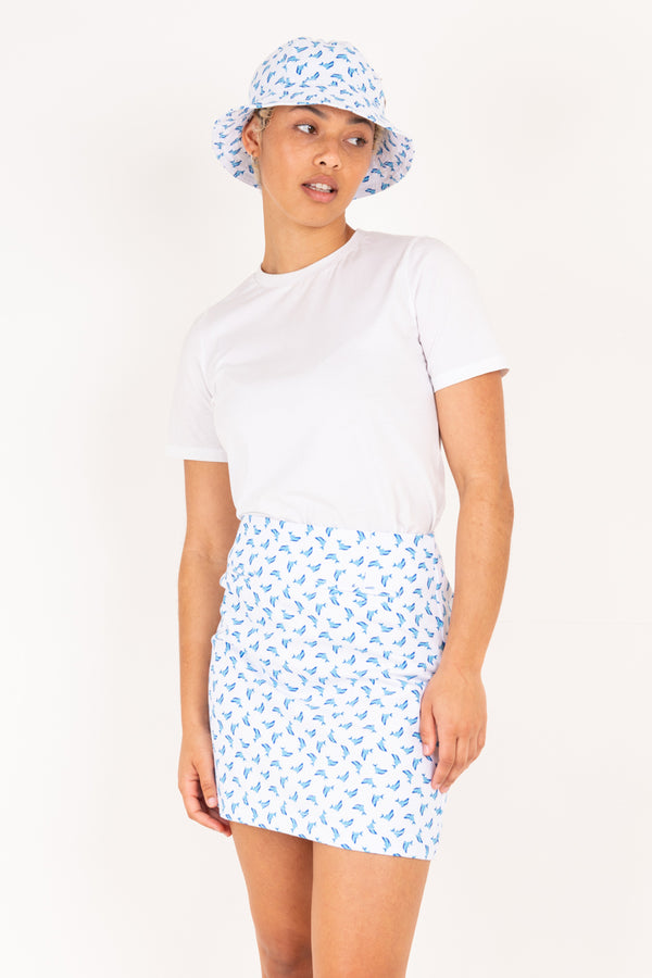Woman wearing a white t-shirt and blue dolphin patterned skirt with a matching hat on a white background