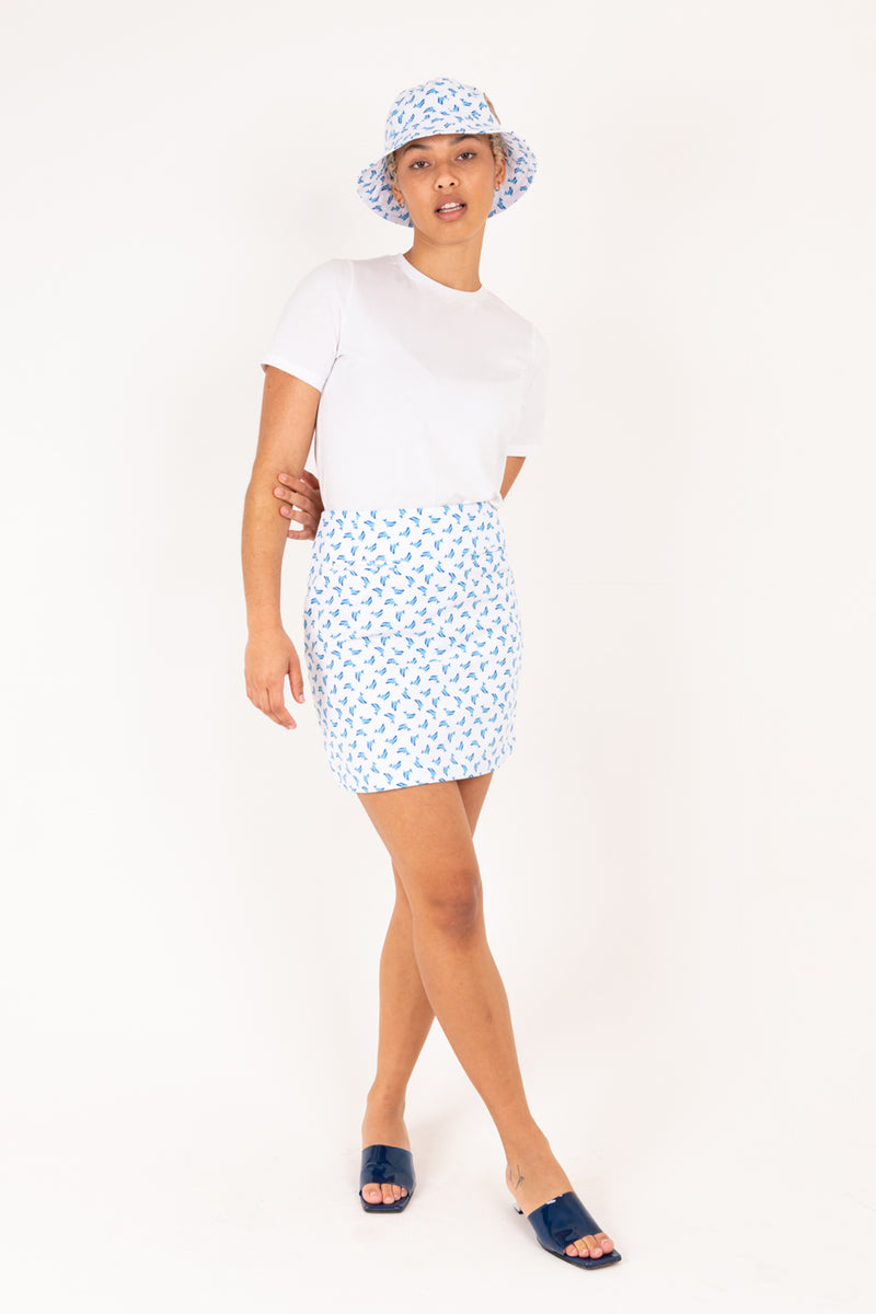 Woman wearing a white t-shirt, blue dolphin patterned skirt, and matching hat on a white background