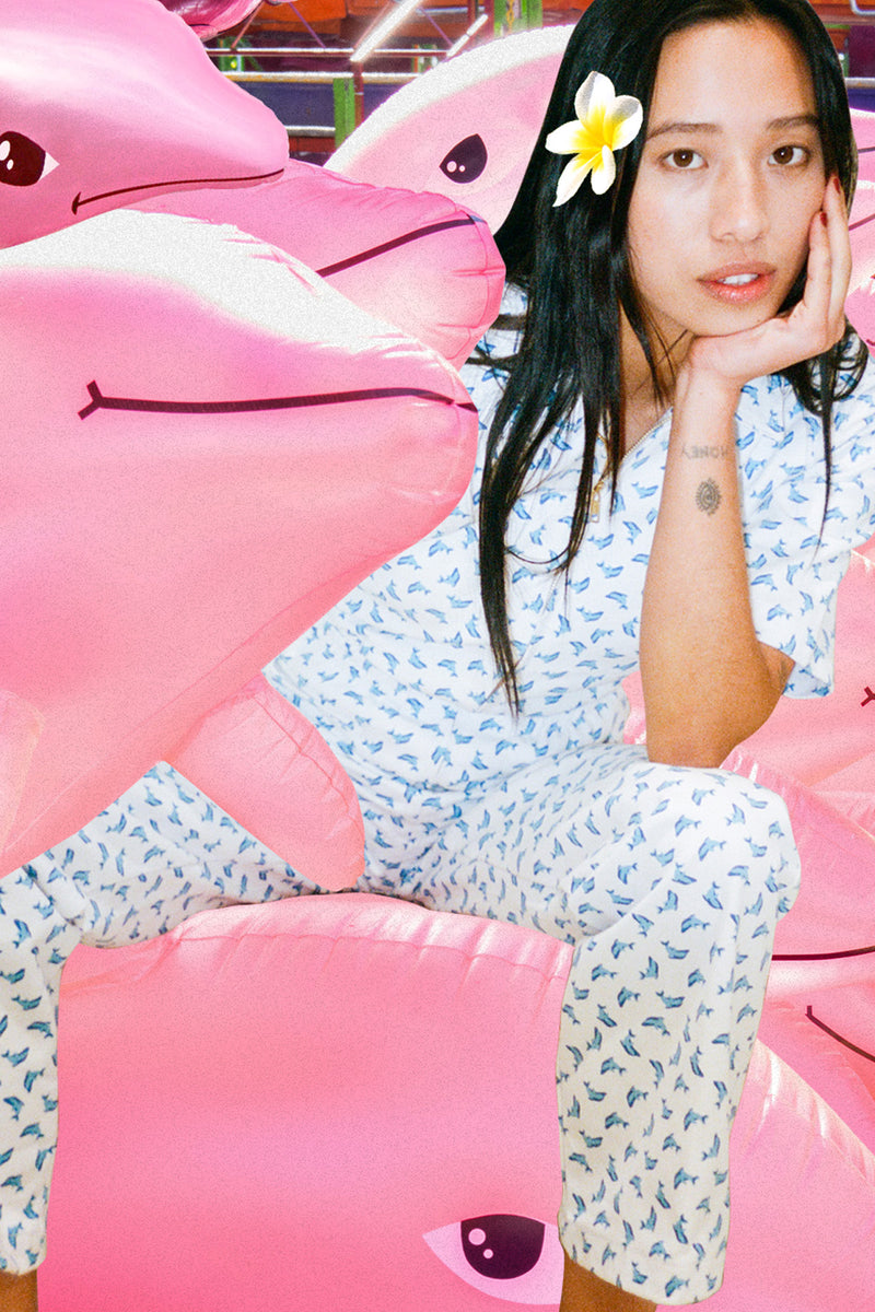 Woman sitting on a pink inflatable shark with a flower in her hair