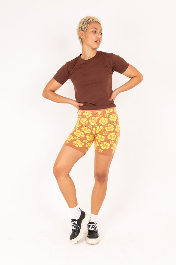 Person wearing a brown shirt and yellow floral shorts on a white background